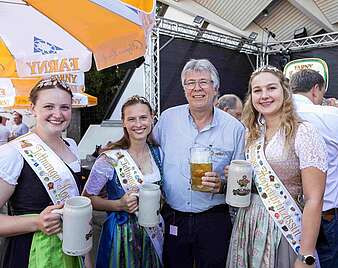 Gruppenbild: drei junge Frauen mit Bierkrügen, Krönchen, Dirndel und Schärpen und Moderator