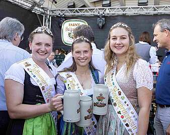 Gruppenbild: drei junge Frauen mit Bierkrügen, Krönchen, Dirndel und Schärpen