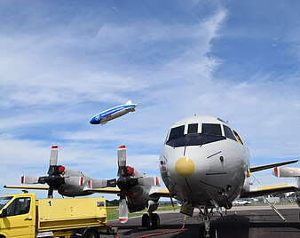 Flugzeug auf Rollfeld von vorn mit Zeppelin fliegend in Hintergrund